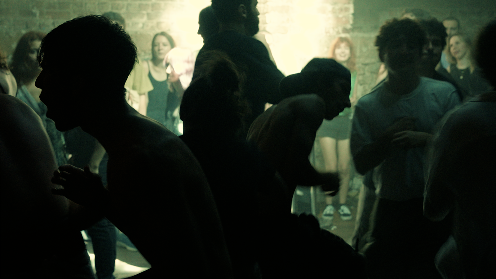 Photo of people dancing in the front and people standing against a wall in the back.